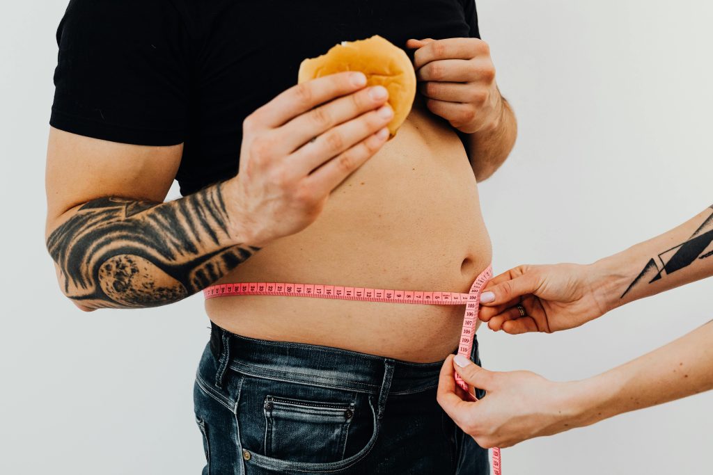 Man holding a burger having their waistline measured