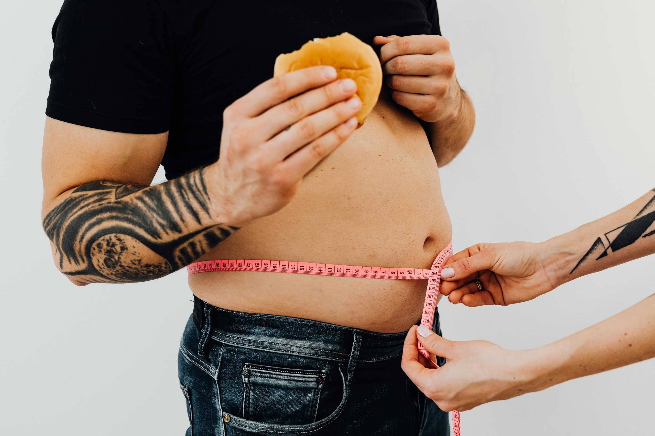 Man holding a burger having their waistline measured
