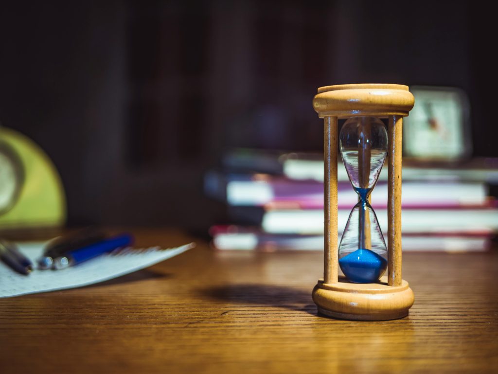 An hourglass with blue sand sitting on a desk